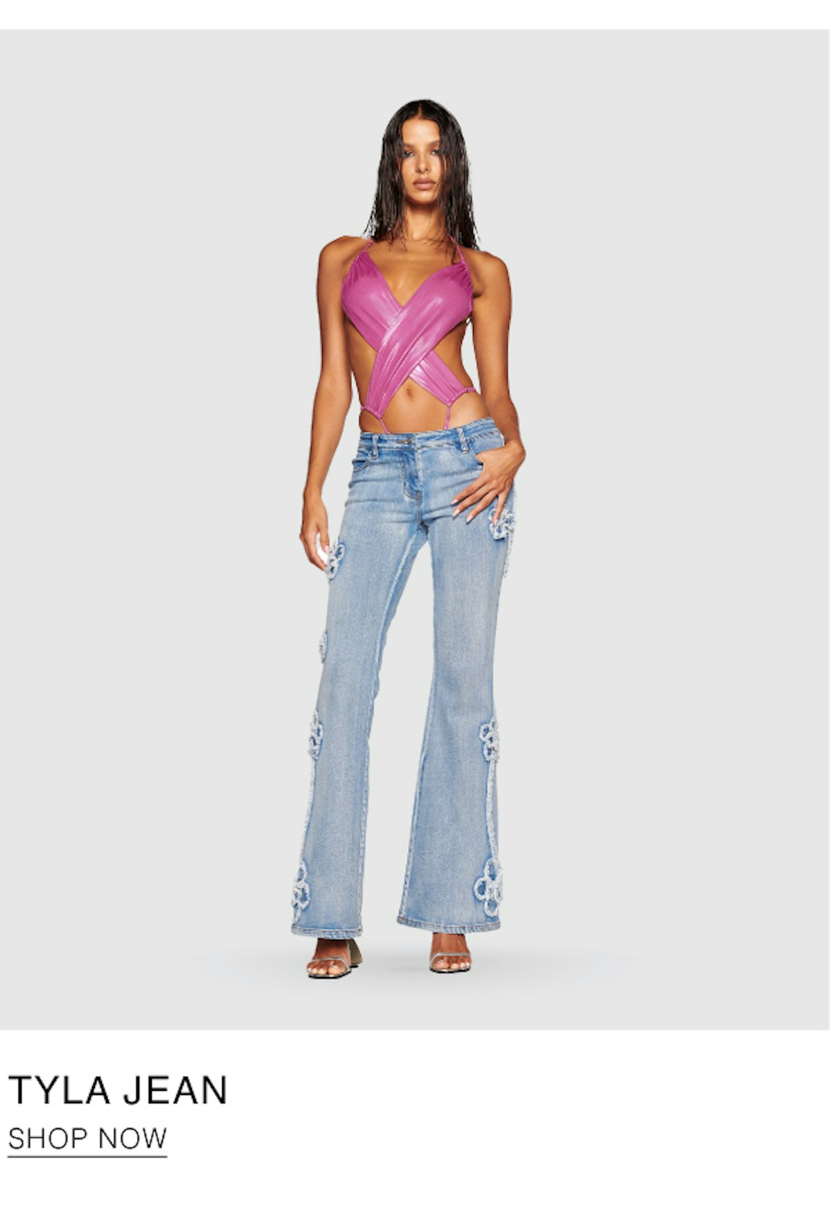 Model wearing pink bodysuit and flared jeans standing in front of grey background.