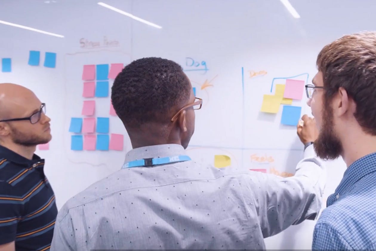 Three men working at a whiteboard using markers and post-it notes