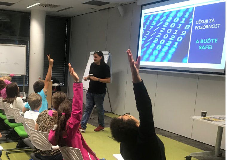 An IBM volunteer in front of an audience of children with their hands raised to answer a question
