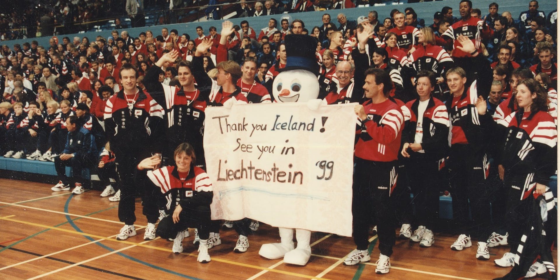 Hópmynd af keppendum frá Liechtenstein á Smáþjóðaleikunum 1997. Inn í miðjum hópnum stendur snjókarl með borða sem á stendur "Thank you Iceland! See you in Leichtenstein´99". Mynd frá ÍSI.