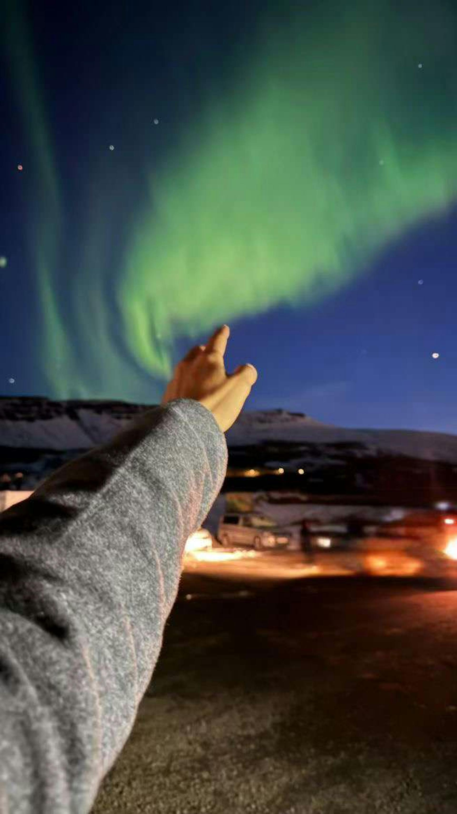 Hand reaching out to beautiful northern lights in Iceland