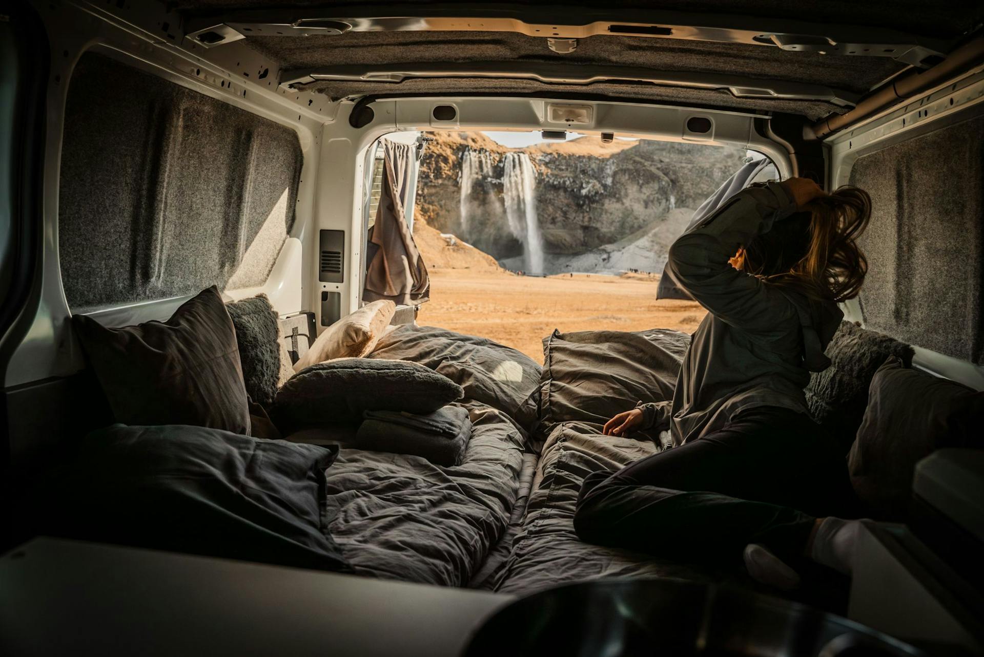 Girl looking outside of campervan bed to Seljalandsfoss waterfall