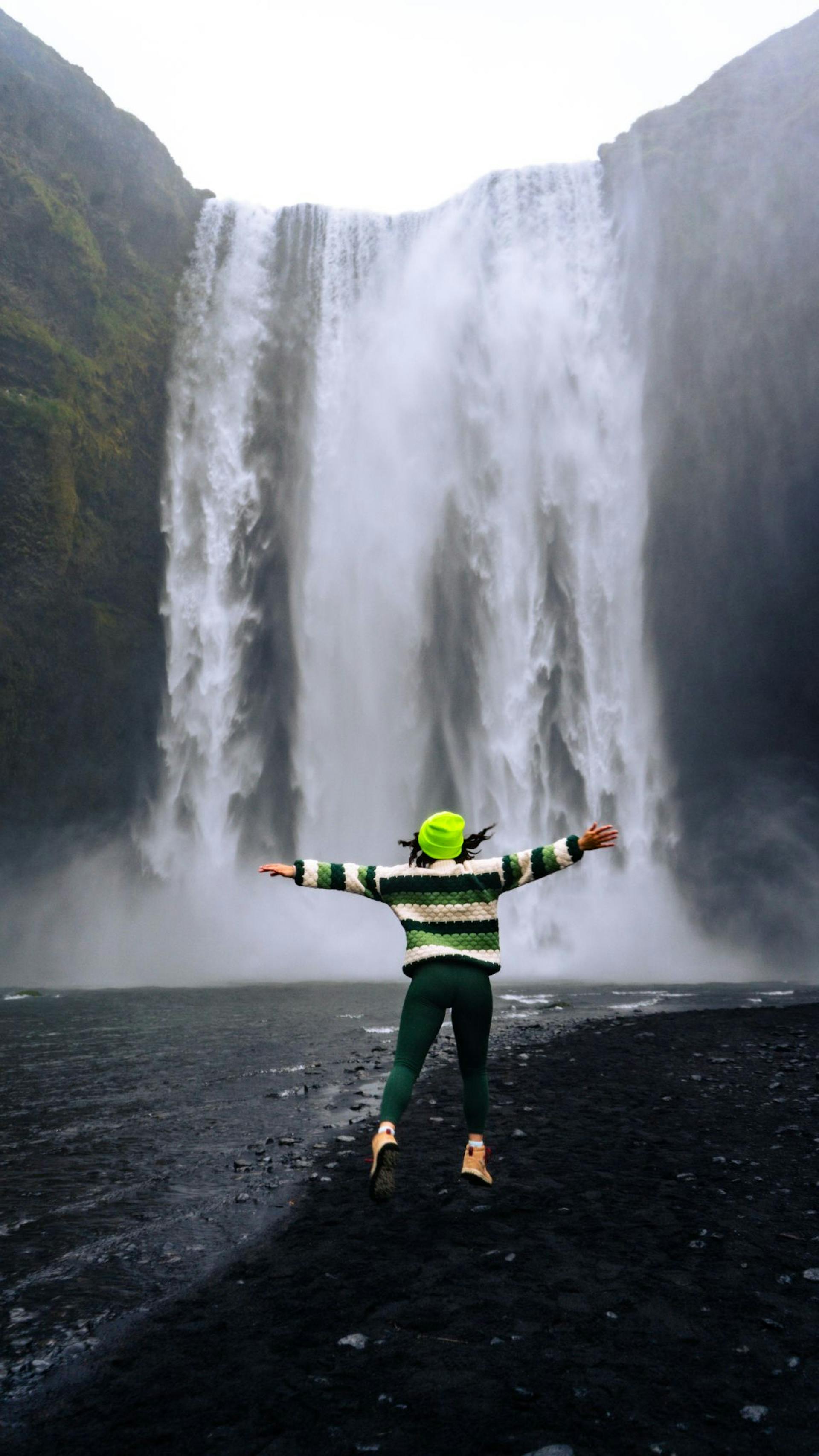 Woman jumping by Skogafoss waterfall in Iceland