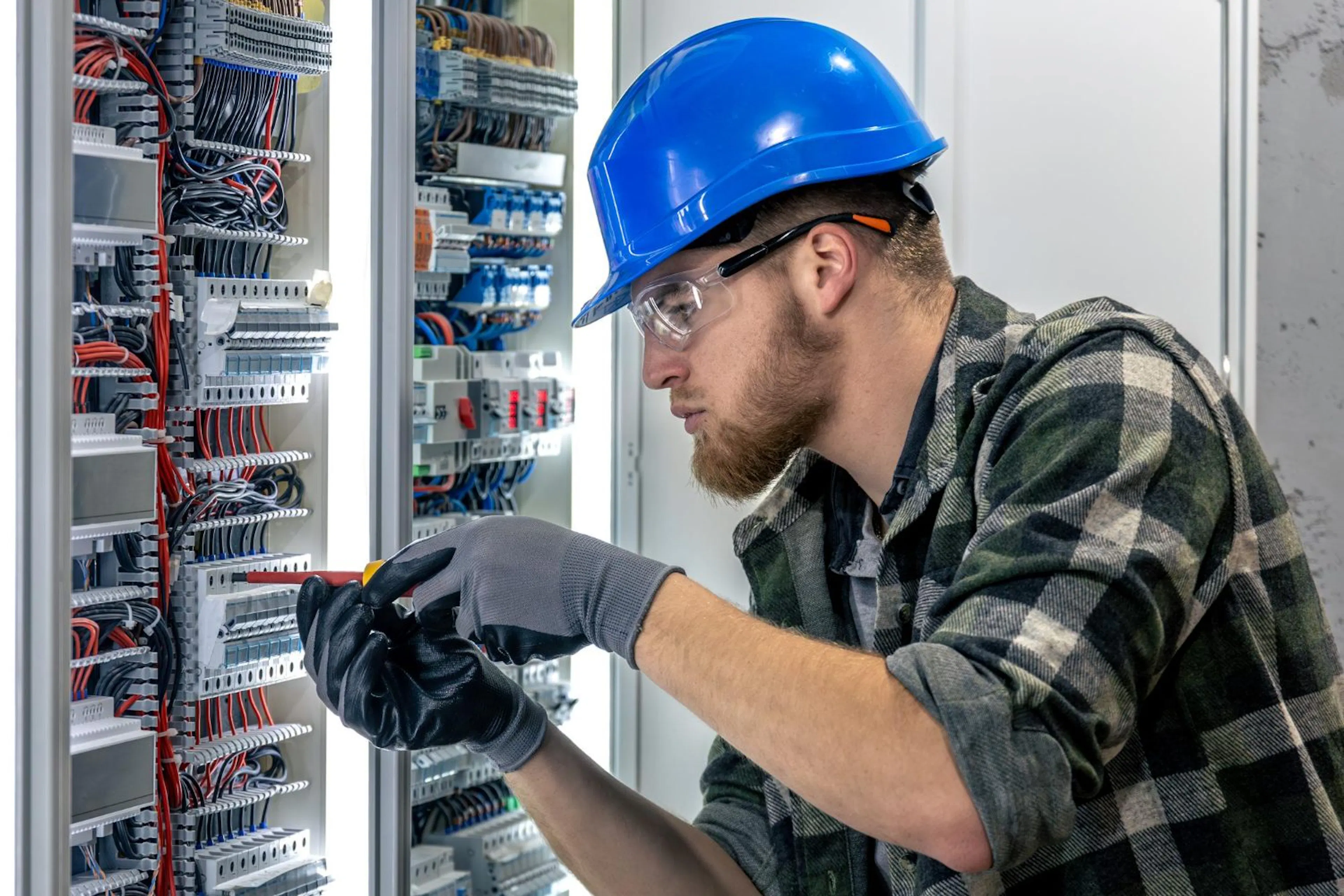 Electrician in a hard hat testing an older switchboard
