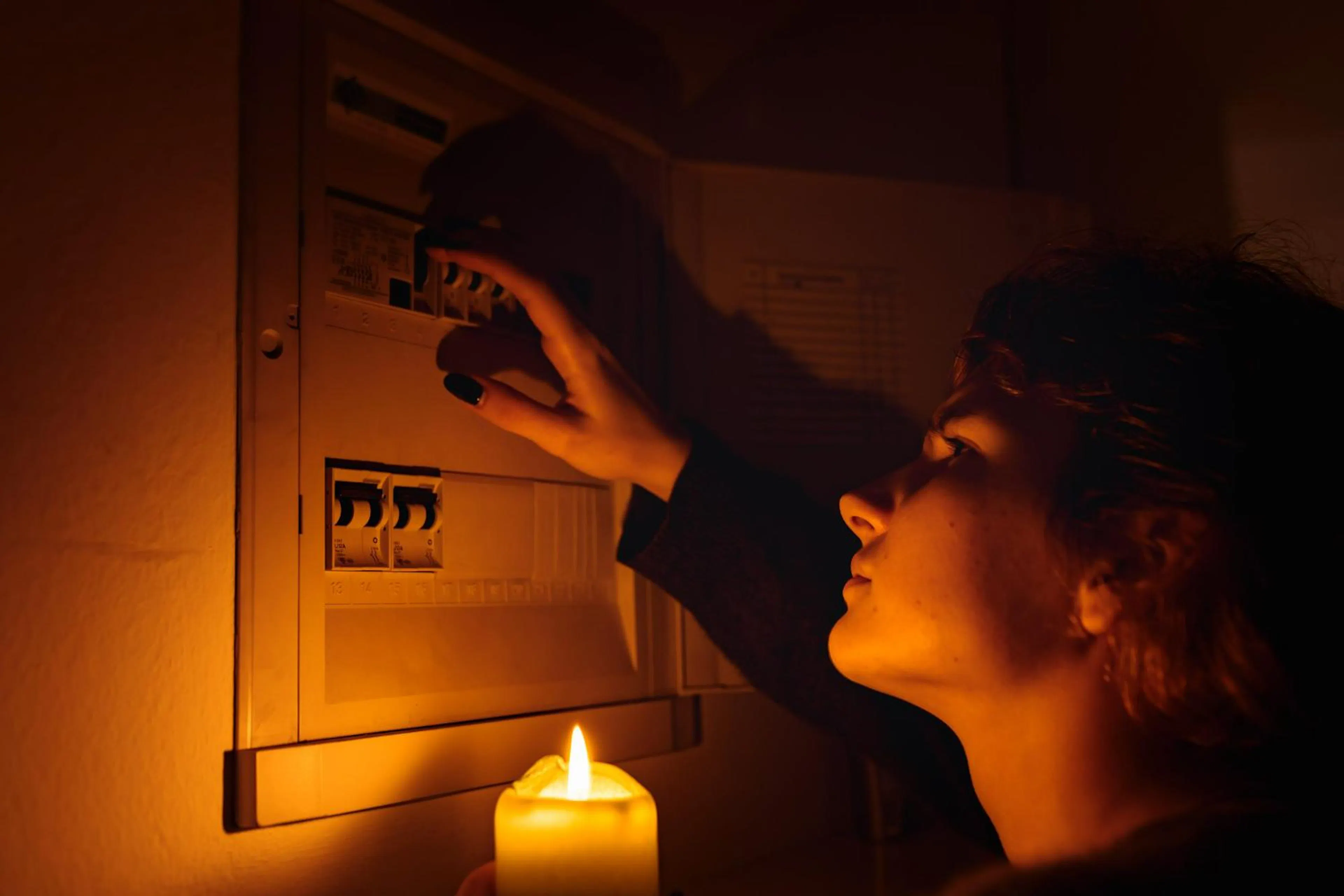Person checking a switchboard by candlelight during a power outage