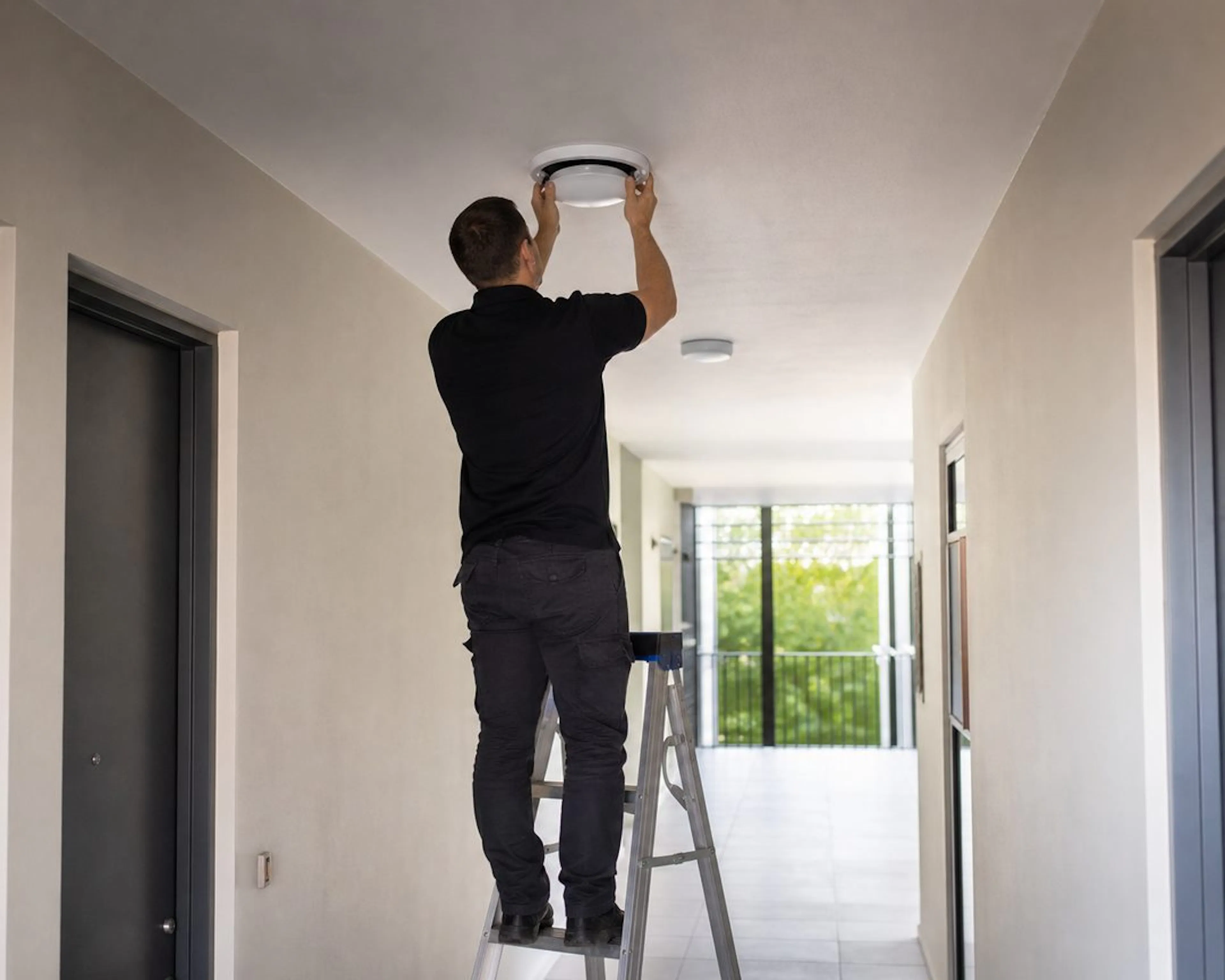 Electrician replacing a common area light in an apartment building corridor