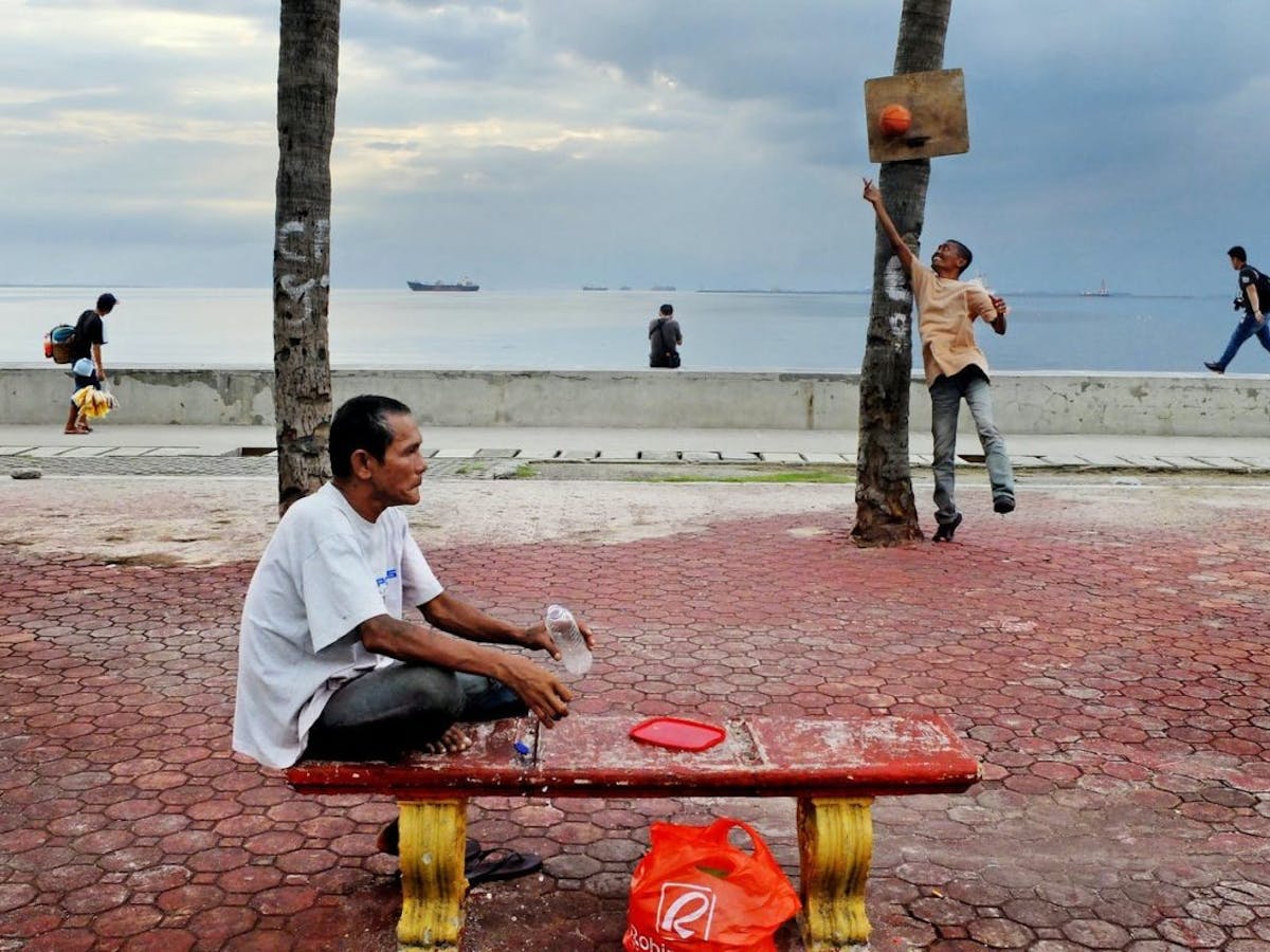 A man cools off with a drink and sea breeze in Baywalk, Manila Bay, Philippines.