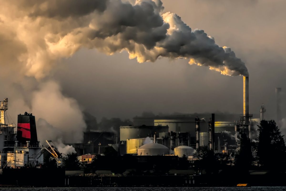 Landscape of ships and smoke coming out of an oil refinery. Photo by Chris LeBoutillier on Unsplash.
