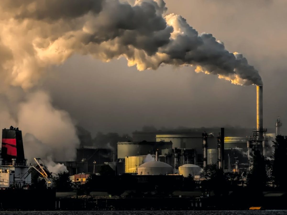 Landscape of ships and smoke coming out of an oil refinery. Photo by Chris LeBoutillier on Unsplash.