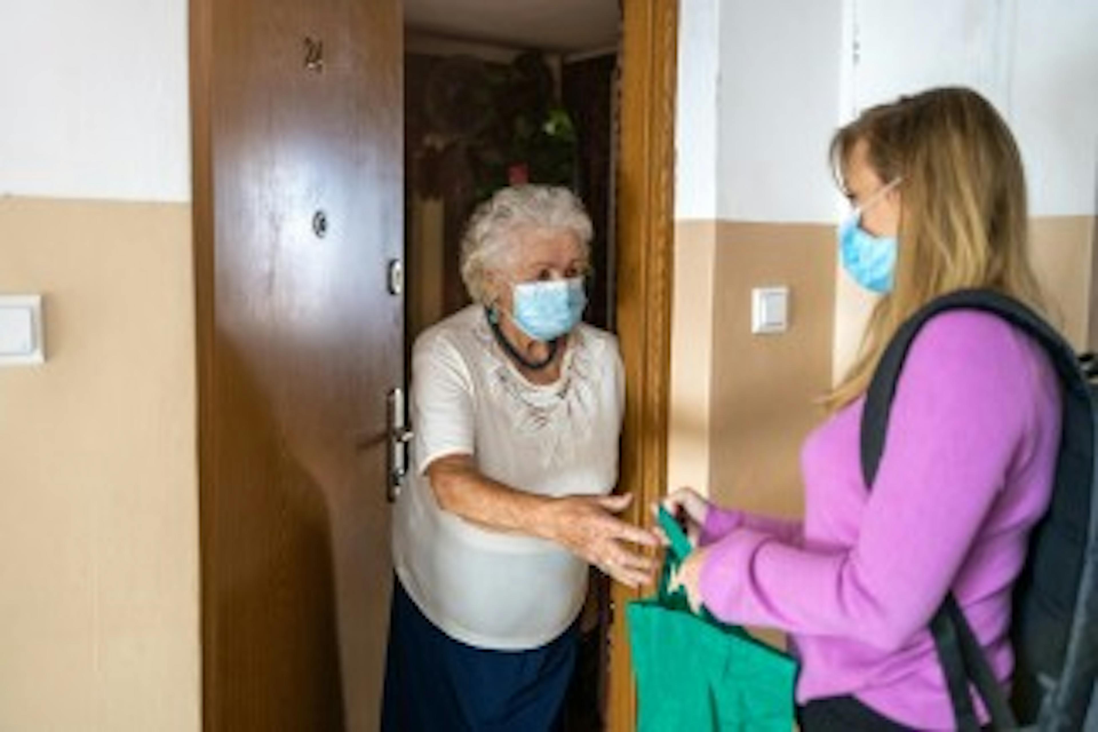 Woman delivering supplies to elderly woman's apartment during COVID-19 pandemic. 