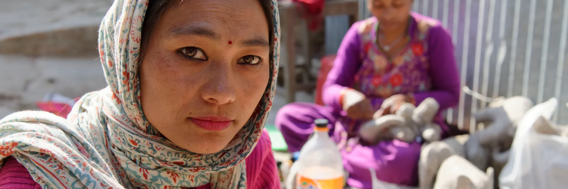 A young Nepali woman looks right at the camera, sitting on the floor of a handicraft production shop in Nepal.