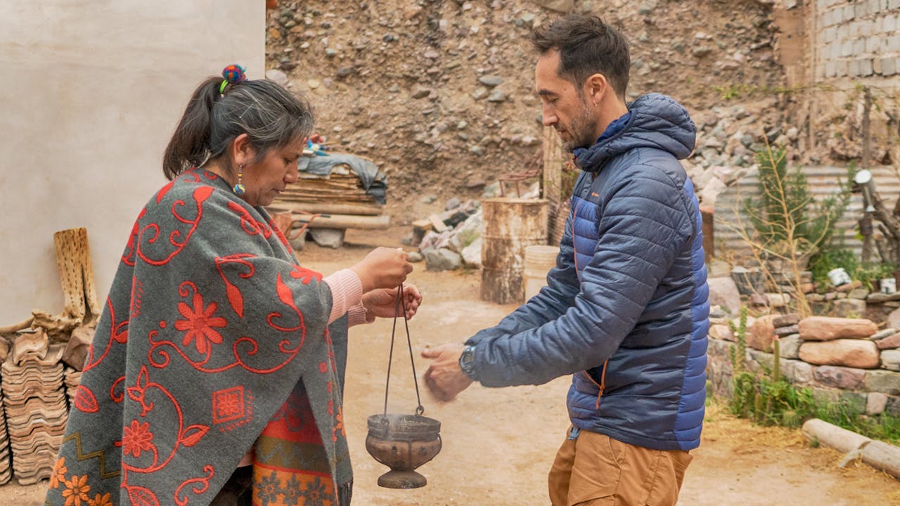 A tourist shreds medicinal herb into a pot held by Celestina.