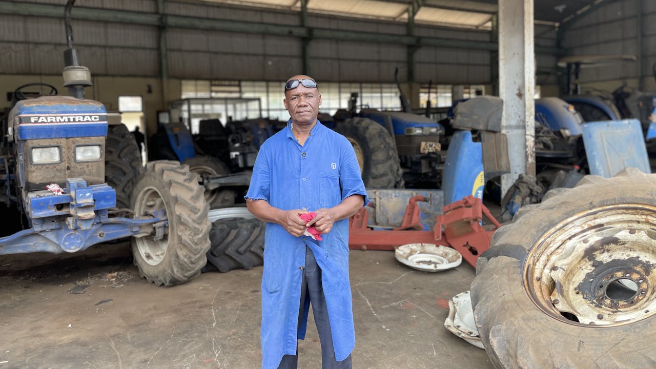Hussein Juma Hassan stands in front of a row of tractors in a warehouse at his workplace.