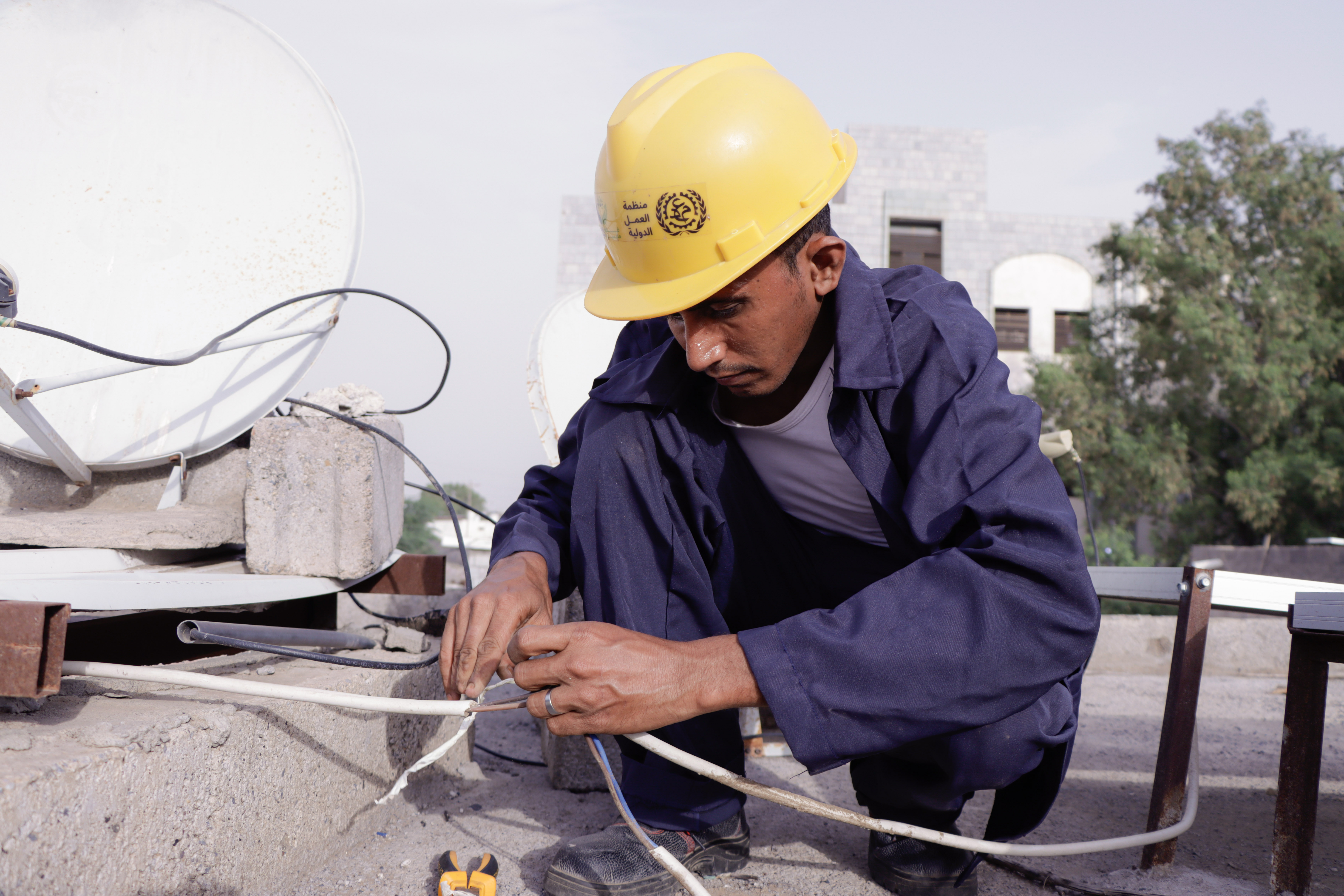 Muhammad Taher Muhammad al-Tahri connects electric cables next to a solar panel on a rooftop.  