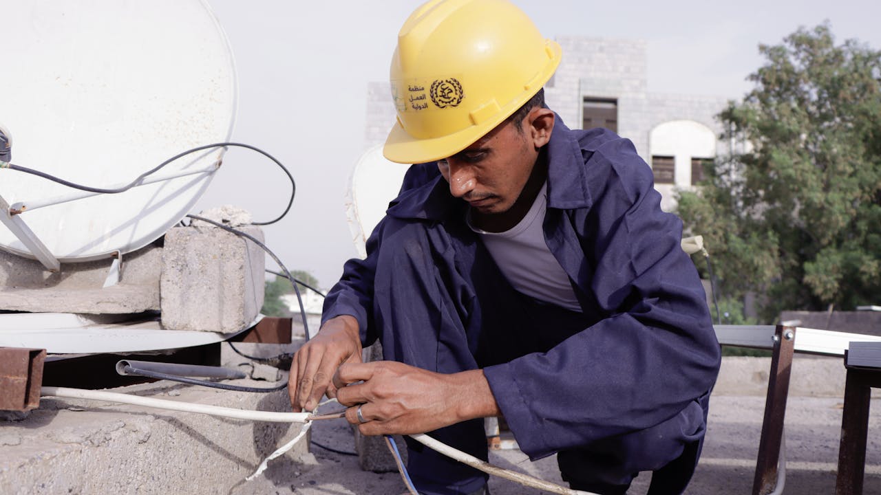 Muhammad Taher Muhammad al-Tahri connects electric cables next to a solar panel on a rooftop.  