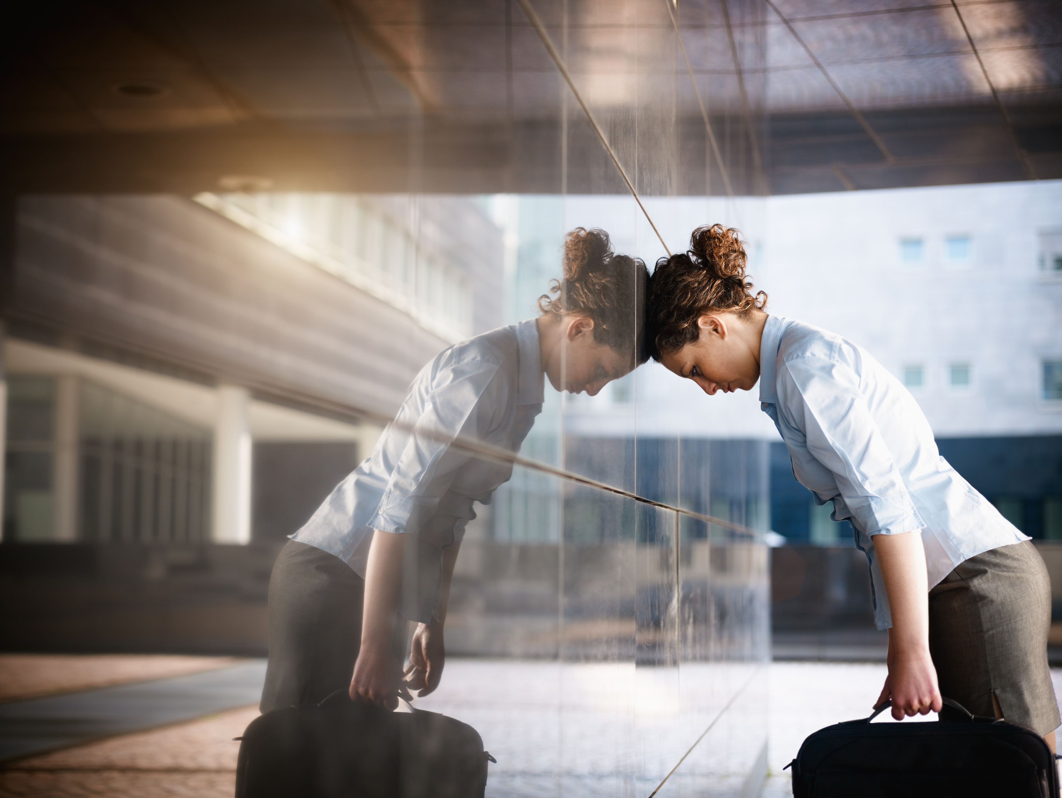 Adult woman leaning her head against a reflective wall outside an office building.
