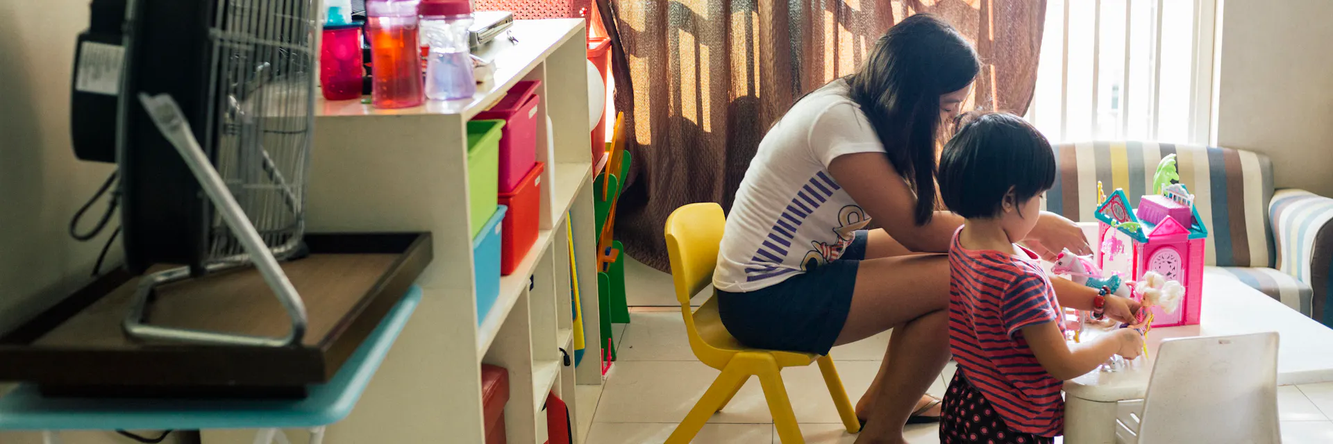 A domestic worker in the Philippines looks after a little girl. They play with dolls.