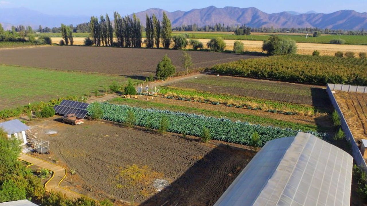 An aerial shot of Alfredo Carrasco’s farm with a greenhouse and fields in the foreground and mountains in the background.