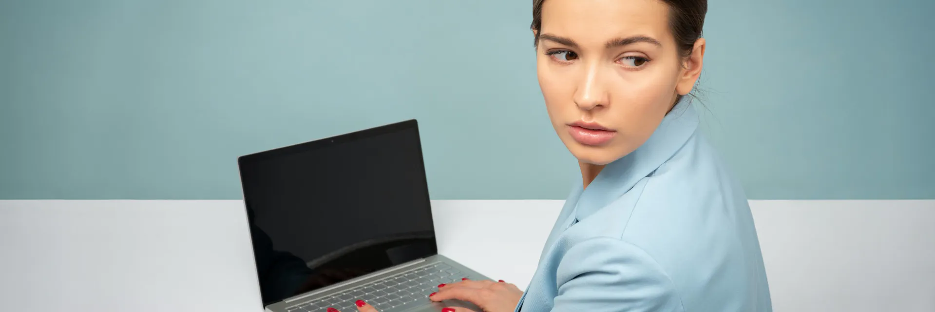 A woman with dark hair sits in front of a computer while looking over her shoulder