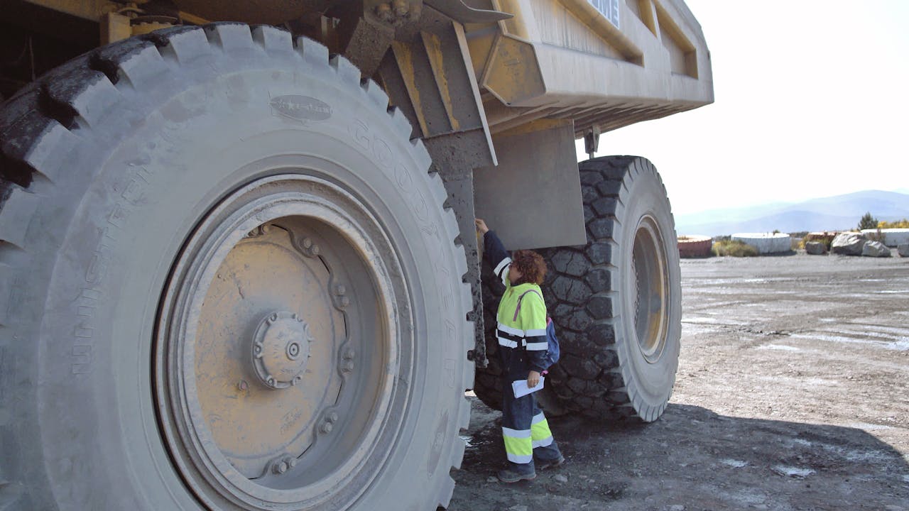 Cristina Carro inspects something on the side of the quarry truck. She is standing between two tyres that are more than twice her height.