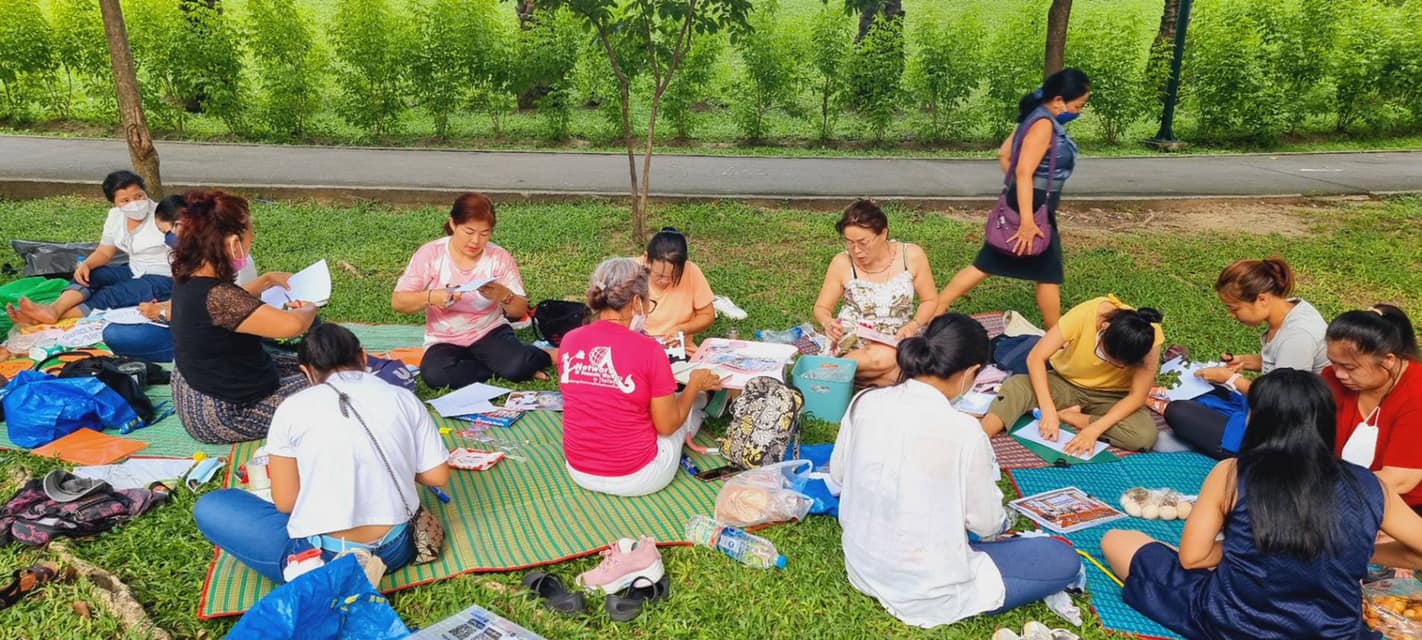 Dans un parc, un groupe de femmes est assis et découpe des morceaux de papier sur lesquels elles écrivent.