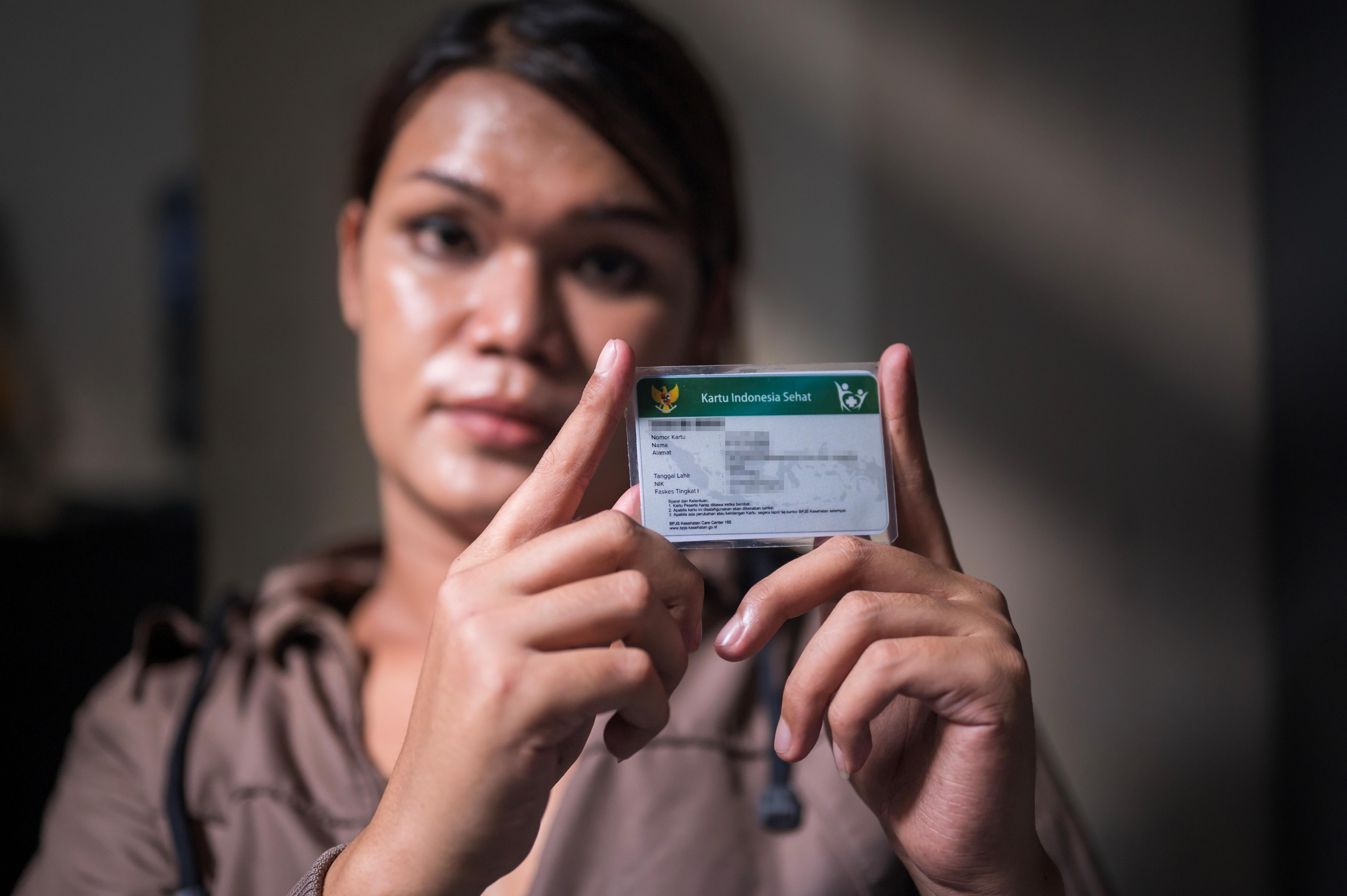 A trans woman holds up her national health insurance card.