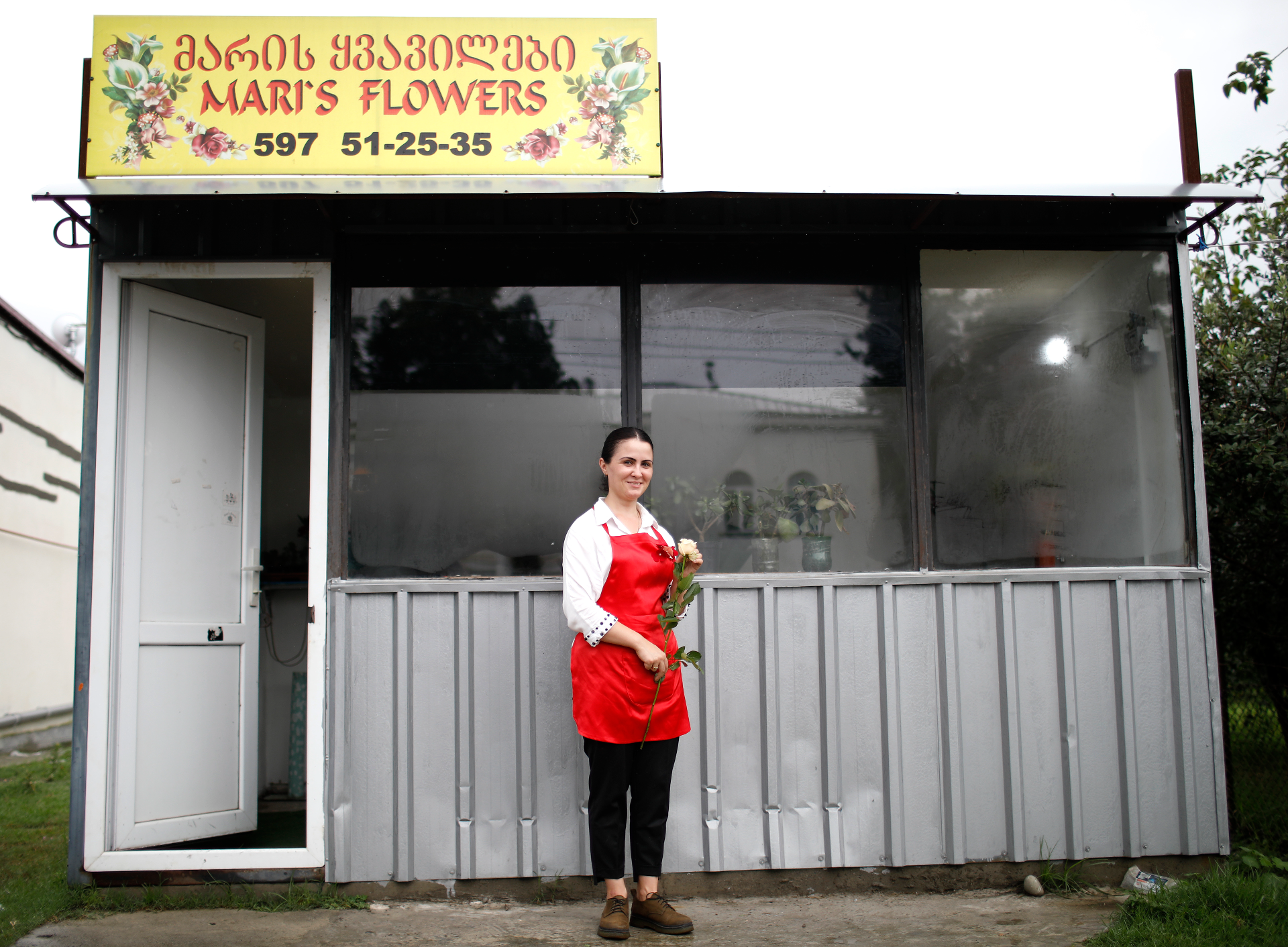 Mariam Kobalia stands in front of her flower shop, "Mari's Flowers" , holding a rose.