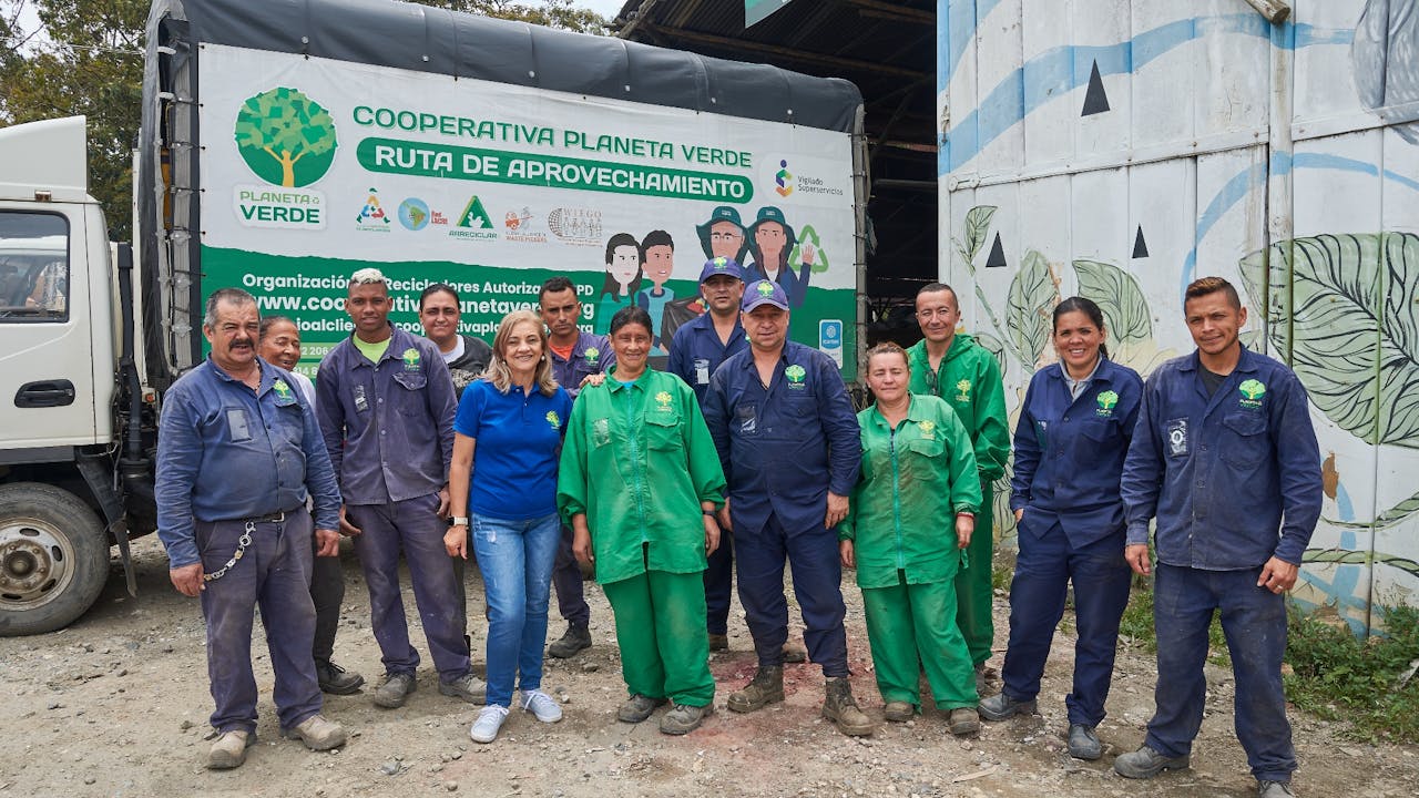 Martha Elena Iglesias poses for the camera with other members of the waste pickers team, in front of one of their waste collection trucks, which has a big sign “Planeta Verde Cooperative”. 