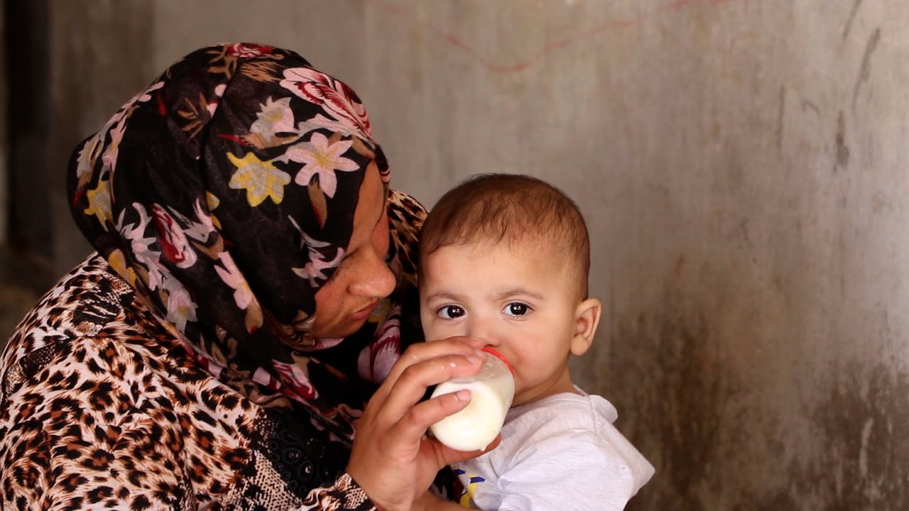 Fatima feeds her baby daughter with a bottle of milk.