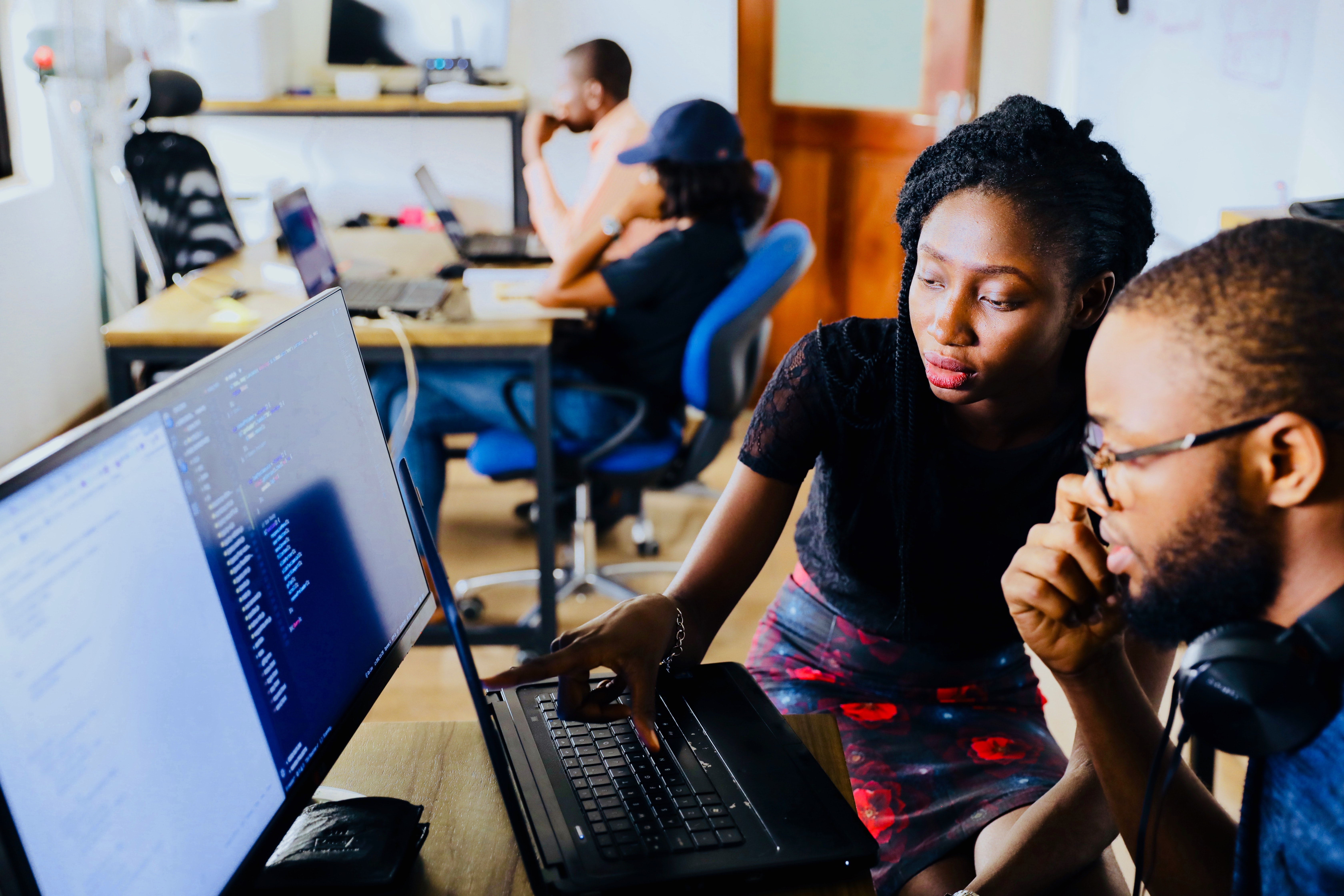 In an open workspace, a woman and man at a pair of large computer screens.