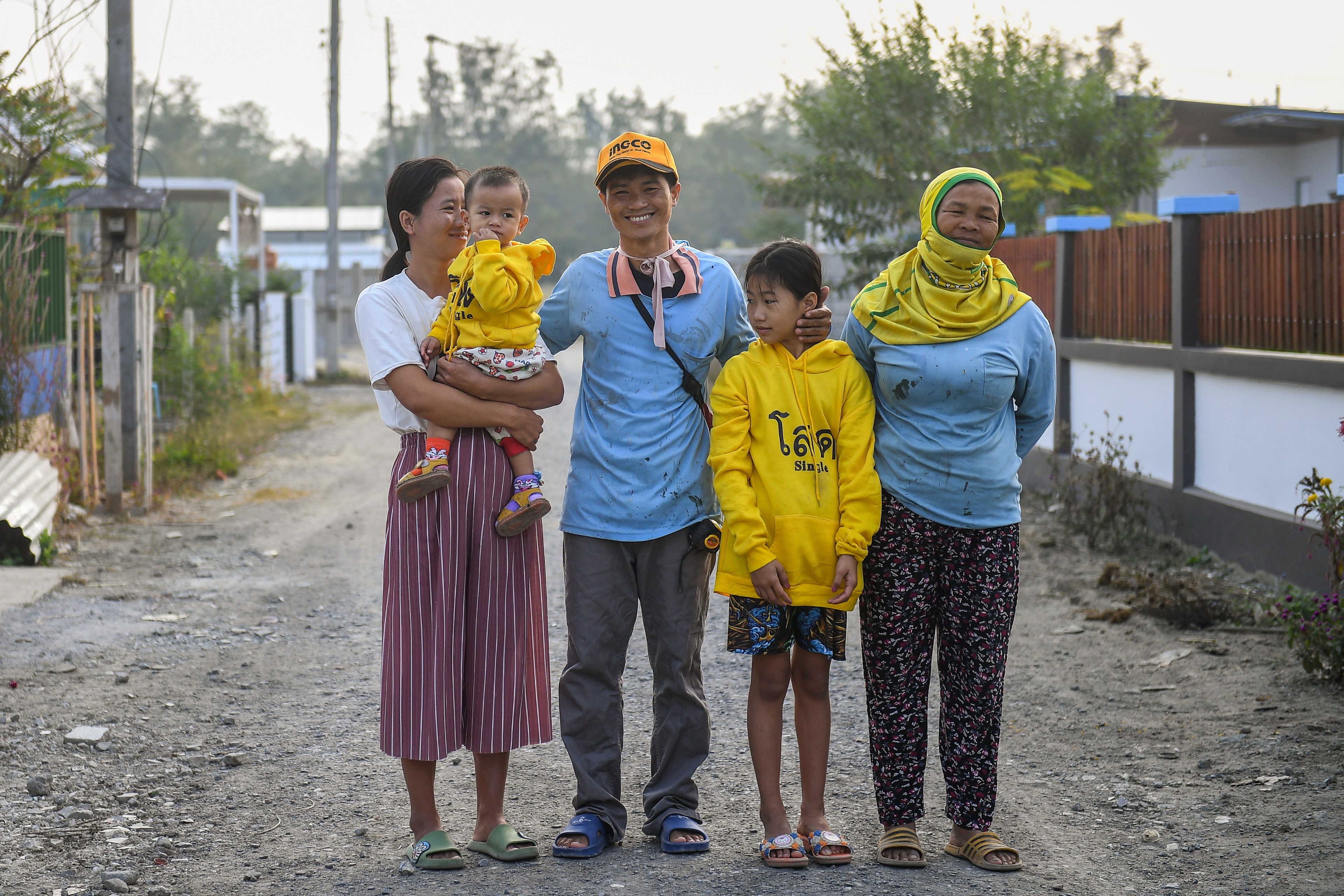 Sai Sai stands on the road with his wife, mother and two children.  He smiles broadly. 