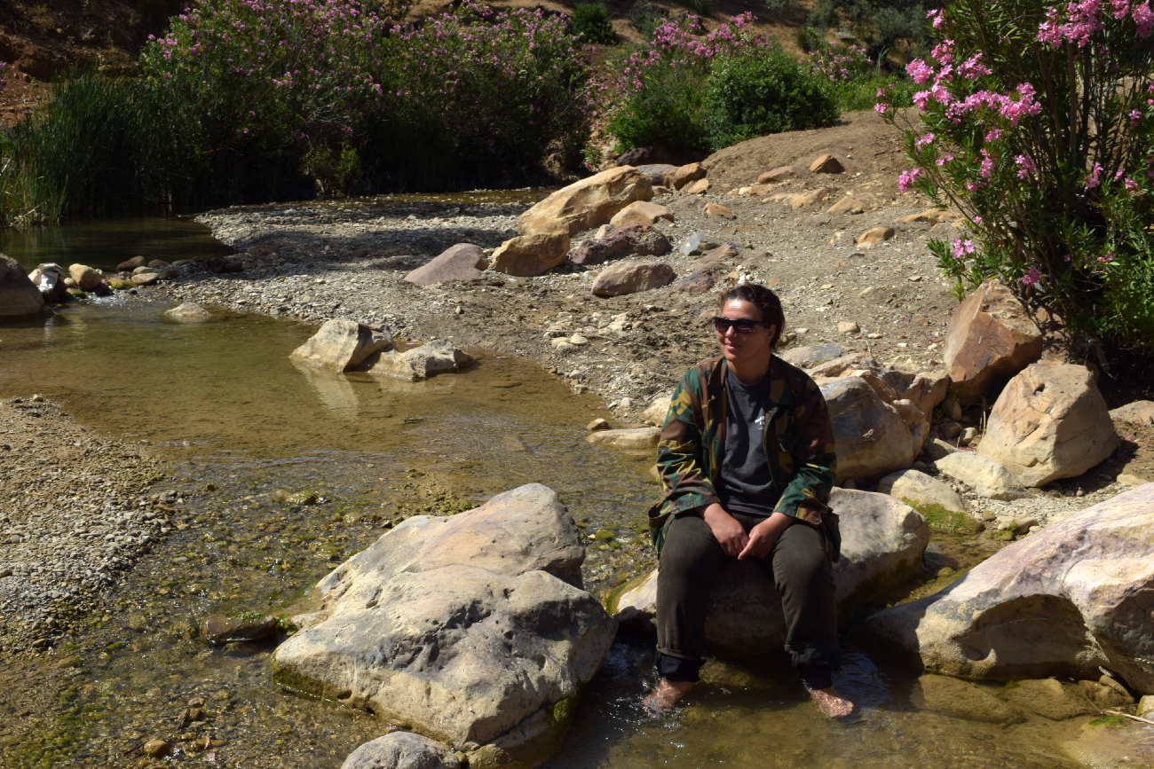 Saida Zouaoui sits with her feet in the water by a brook.