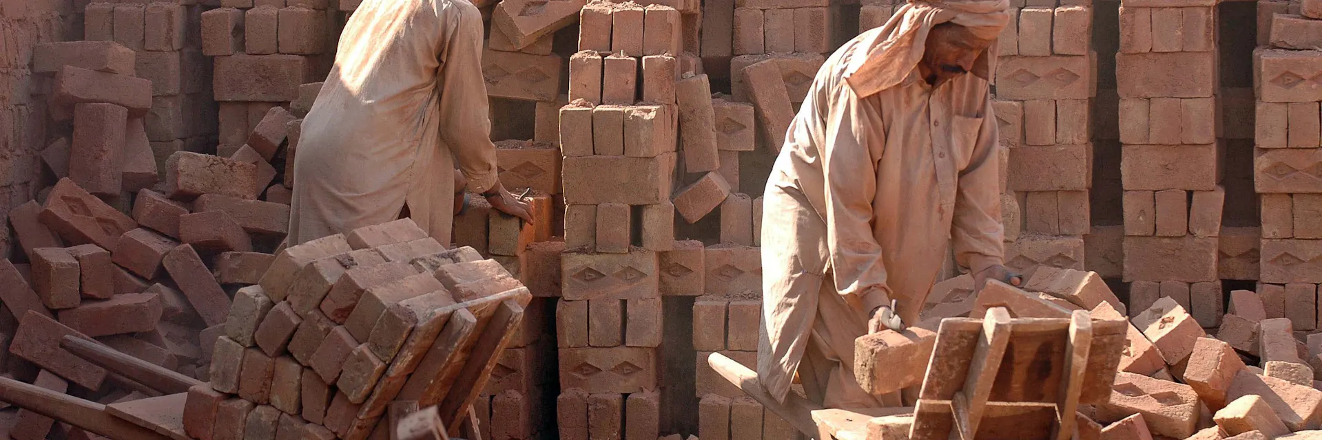 Two male workers in bonded labour move bricks at a brick factory near Islamabad, Pakistan.