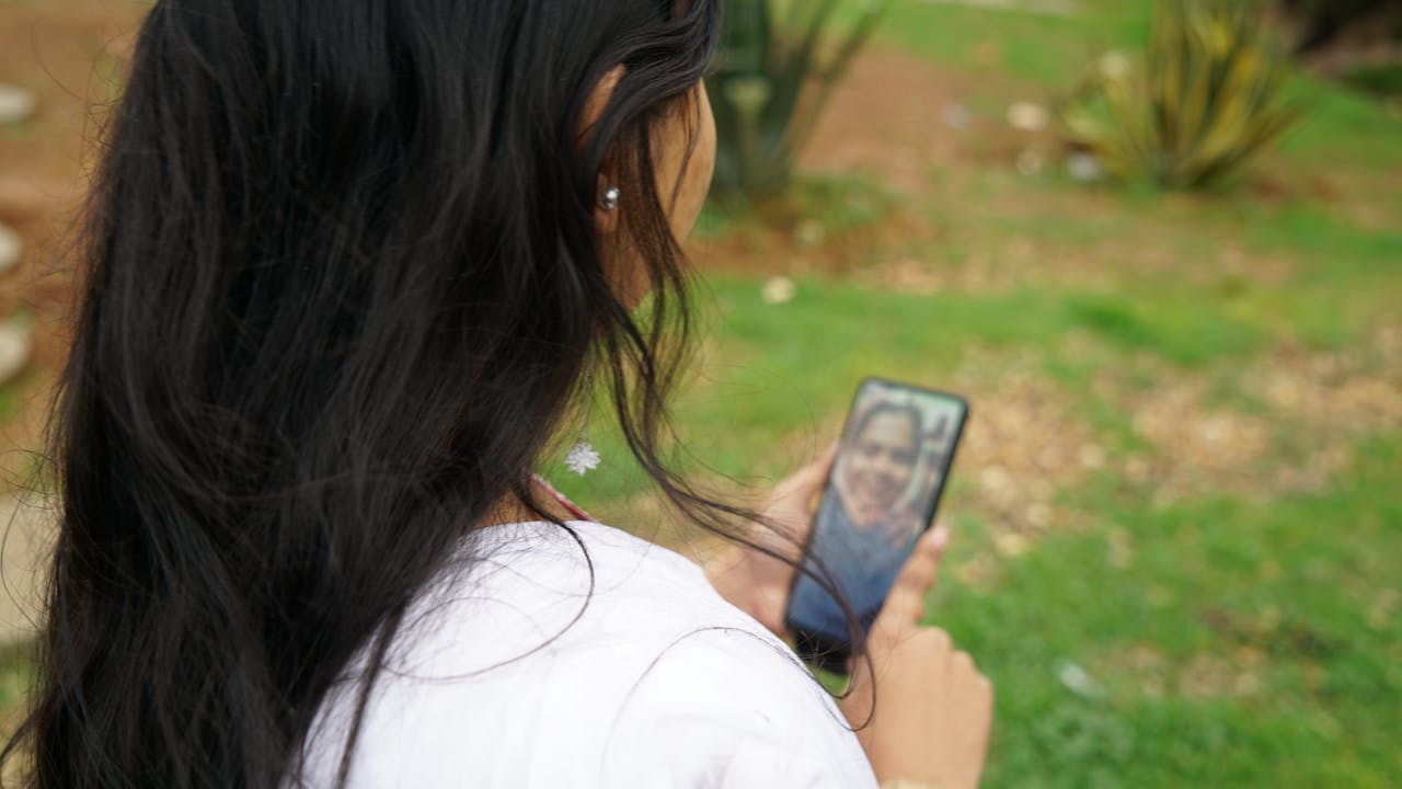 Maya speaks to a family member on a video call from her smartphone.  We see the face of a woman on the phone screen.