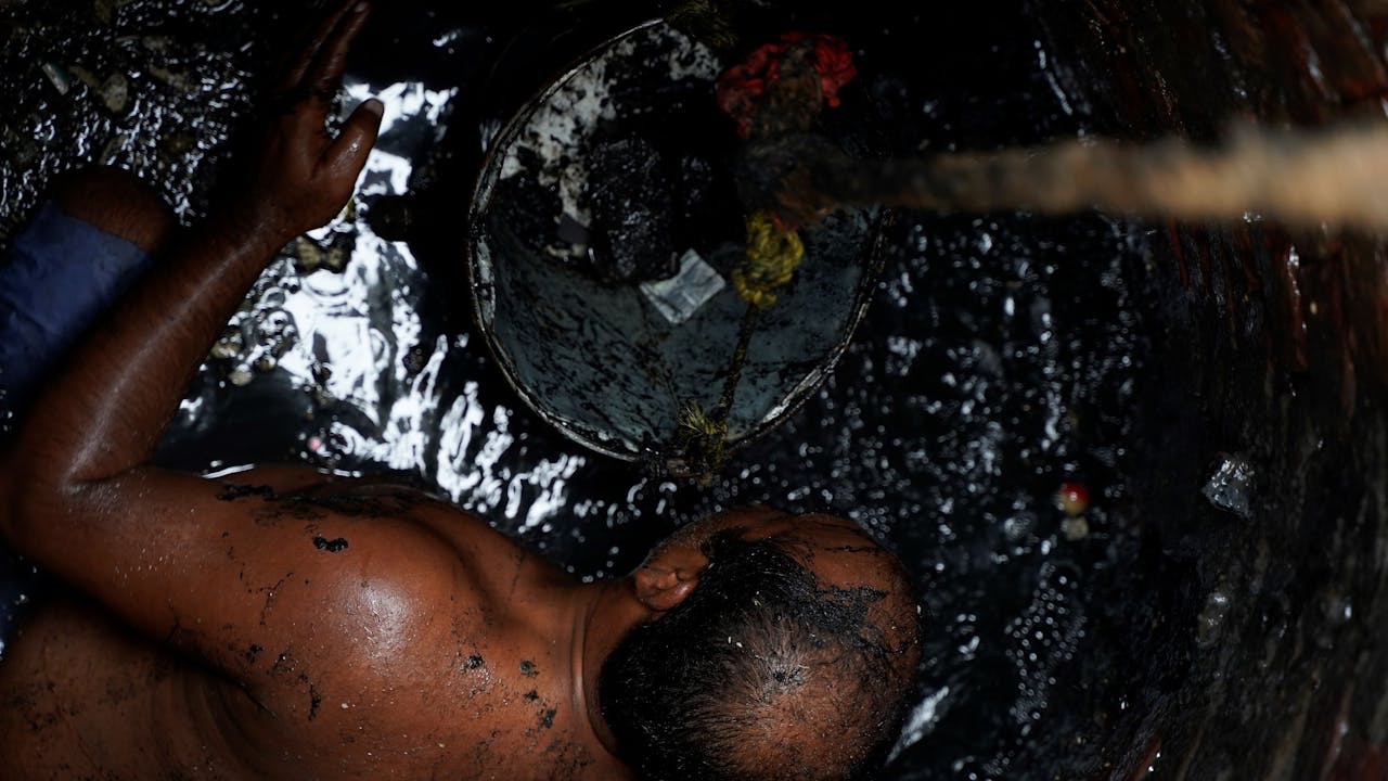 Shafique Massih trabajando en una alcantarilla, sin camiseta, entre aguas residuales. 