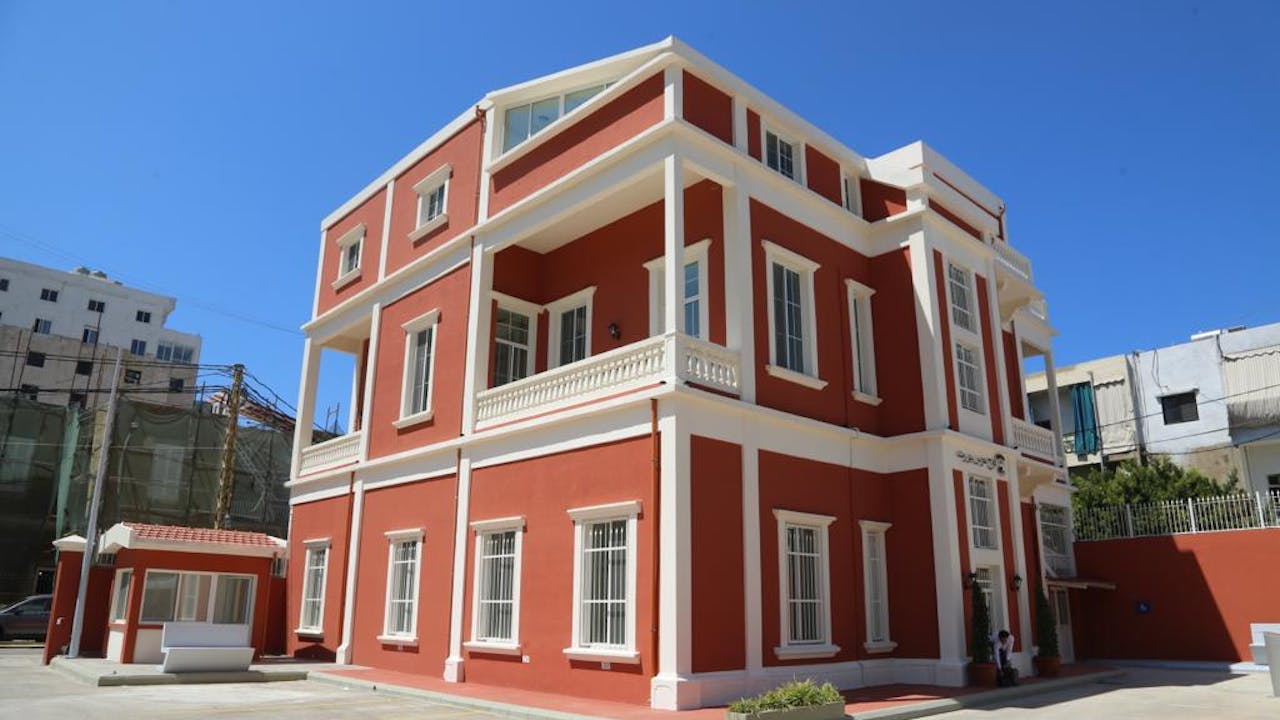 The exterior of the municipal police station after the rehabilitation work. The building’s paintwork has changed to a rich red brick colour with white trim. 