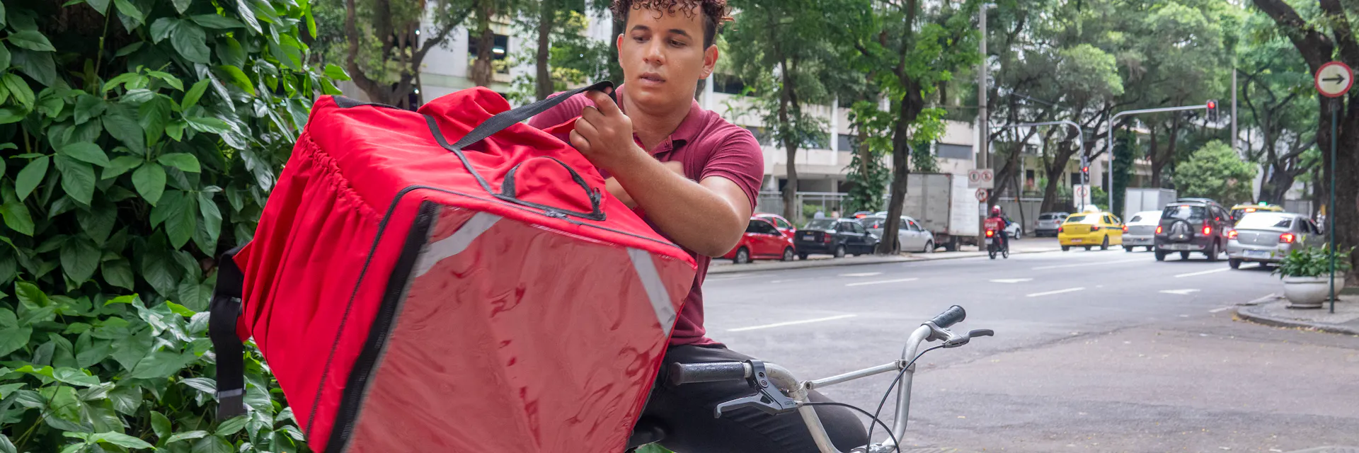 El repartidor se quita la mochila de la espalda para entregársela al cliente.