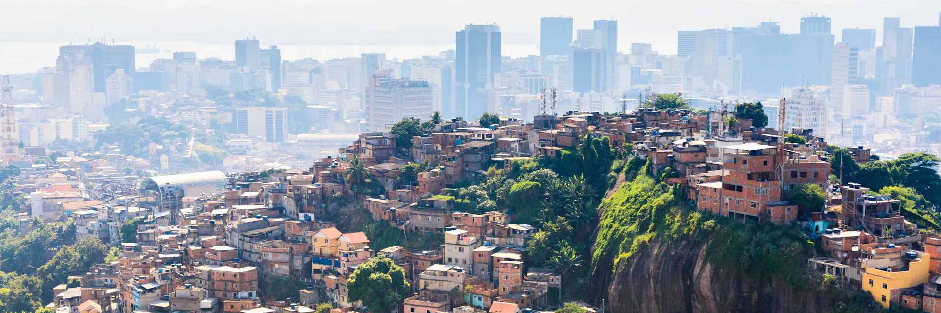 Working-class neighborhoods know as favelas line the side of a hill in Rio de Janeiro, Brazil. In the background we see modern high-rise buildings of the affluent downtown part of the city.