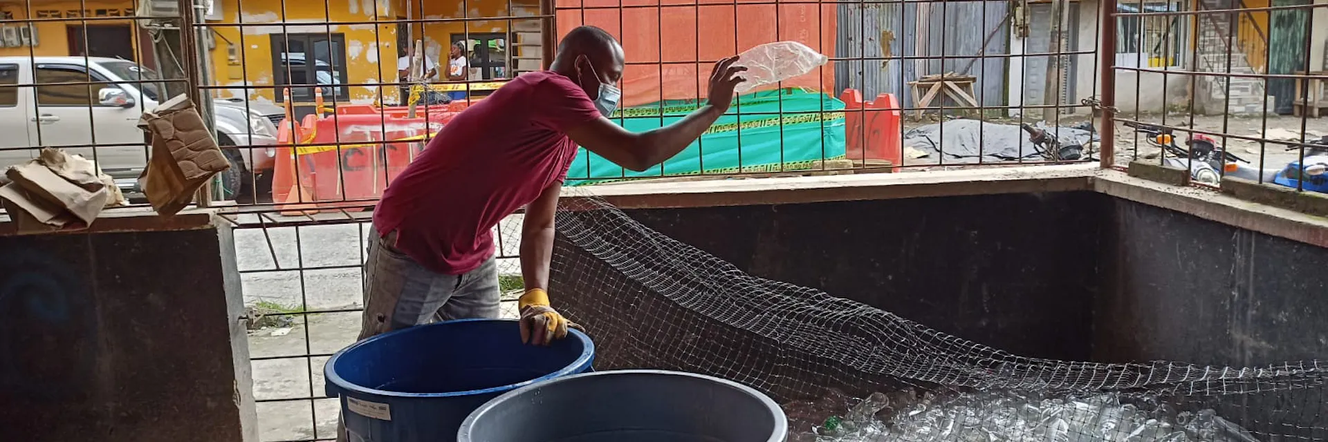 Joven negro arrojando una botella vacía a un montón de otras botellas vacías