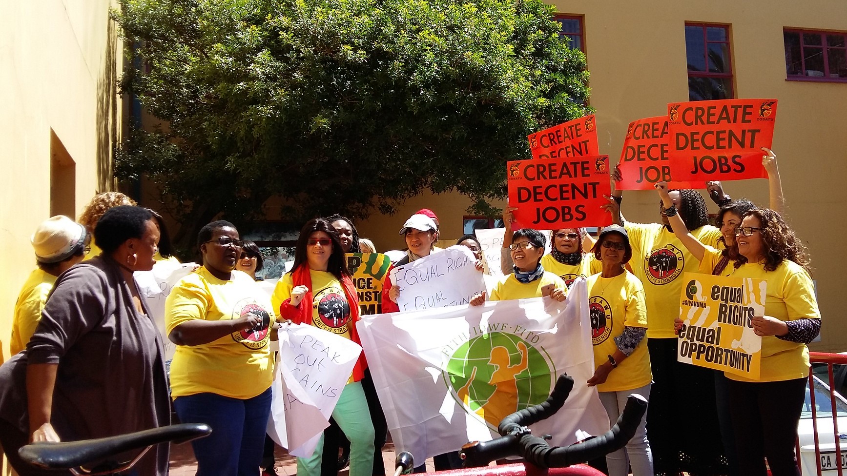 Domestic workers in South Africa in 2017 at a rally, stand outdoors and hold up signs which read: "CREATE DECENT JOBS". 