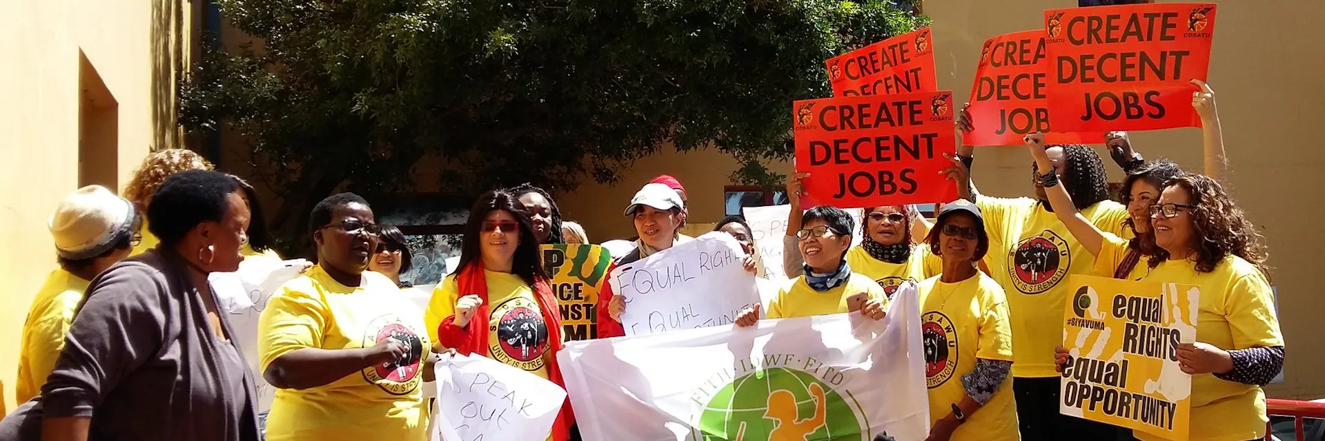 Domestic workers in South Africa in 2017 at a rally, stand outdoors and hold up signs which read: "CREATE DECENT JOBS".