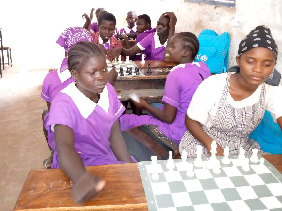 Varias niñas con uniforme escolar de color púrpura juegan al ajedrez.