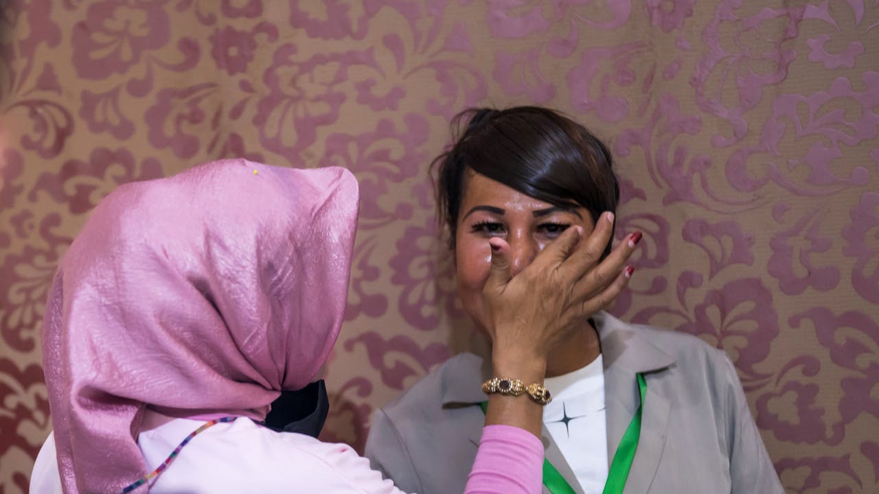 Someone wearing a pink headscarf uses her finger to adjust Echi’s eye make-up.