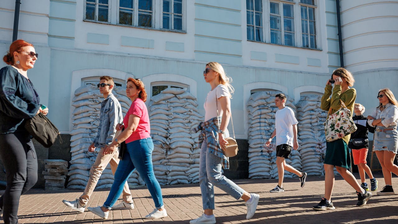 Personas en Kiev, capital de Ucrania, caminan junto a un edificio con sacos de arena apilados frente a sus ventanas.