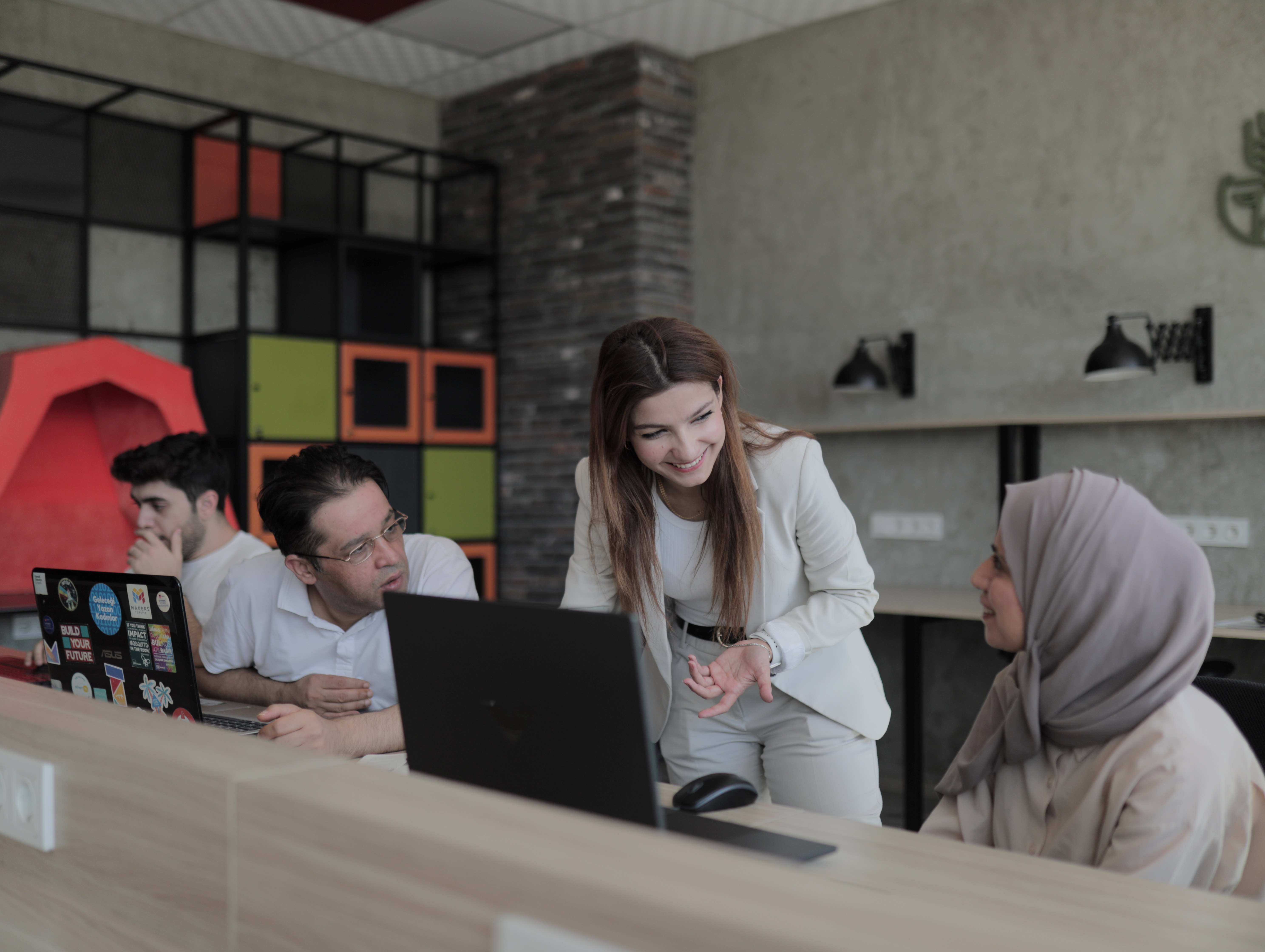 Jin Dawod speaks to two colleagues in an office space. Another colleague looks at a computer screen. 