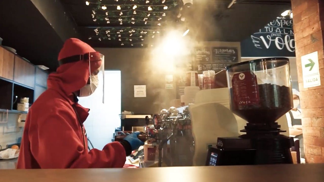 One of the employees prepares coffee and wears personal protective equipment and clothing  to avoid contagion. 