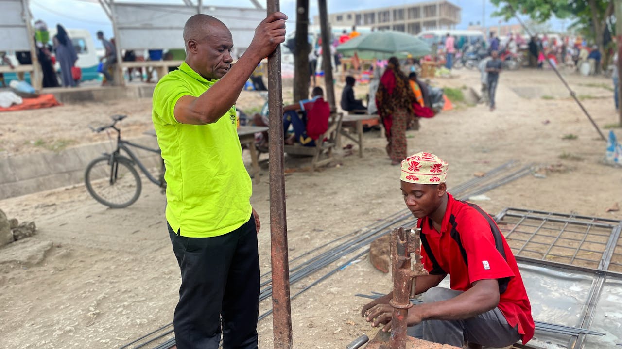 Hussein Juma Hassan observes the work of a young employee at his welding business.