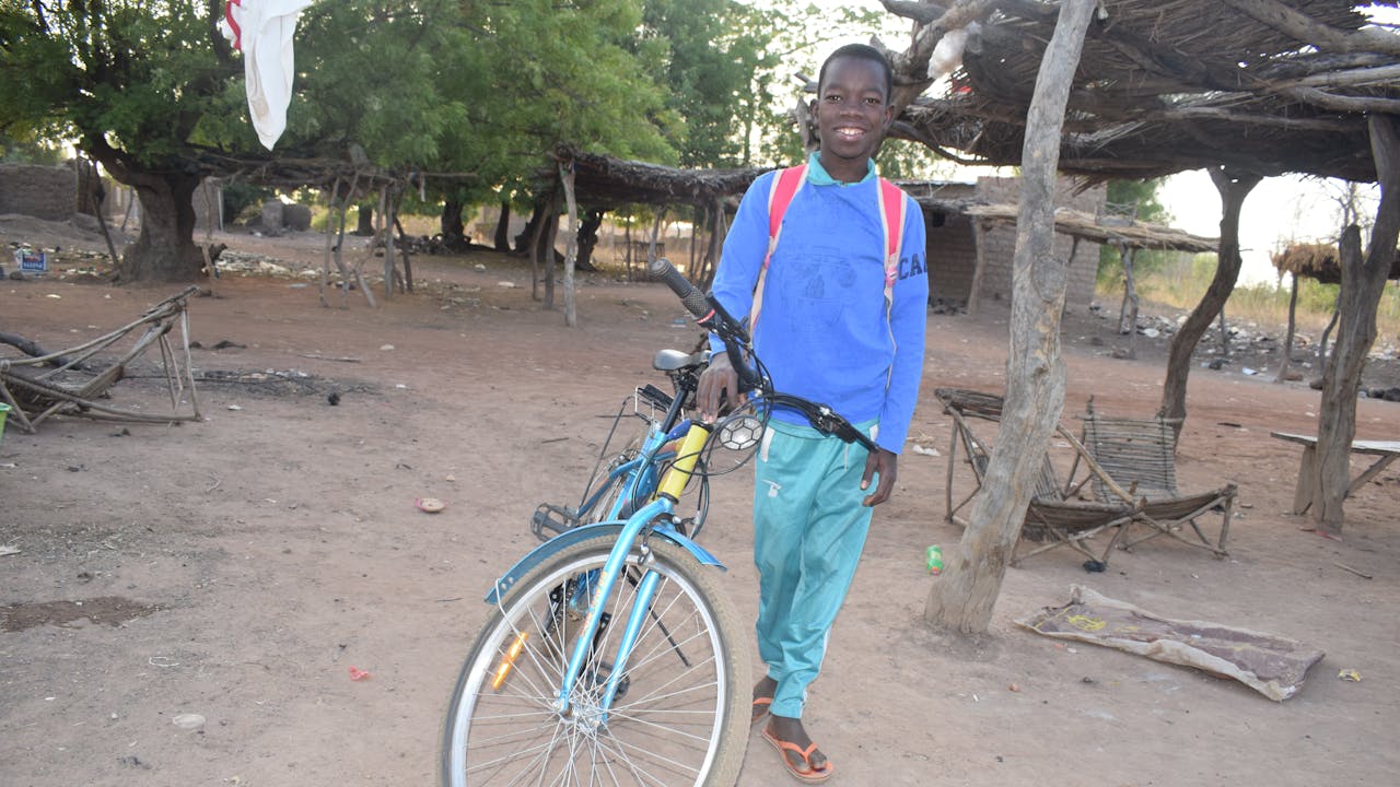 Domboué Nibéissé stands next to a bike and smiles.