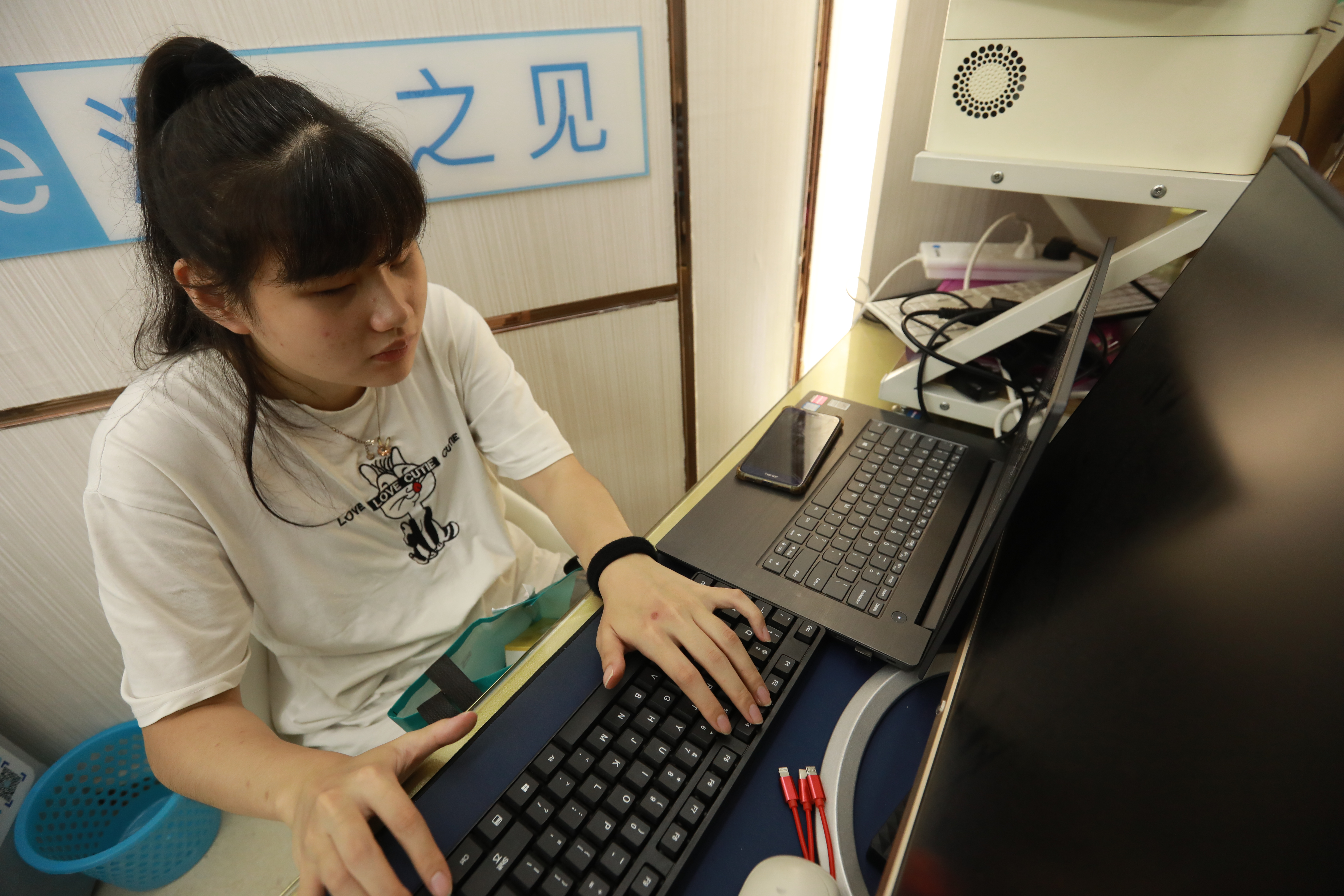 Small Wolf sits at a desk in front of a computer.  She types on a keyboard.