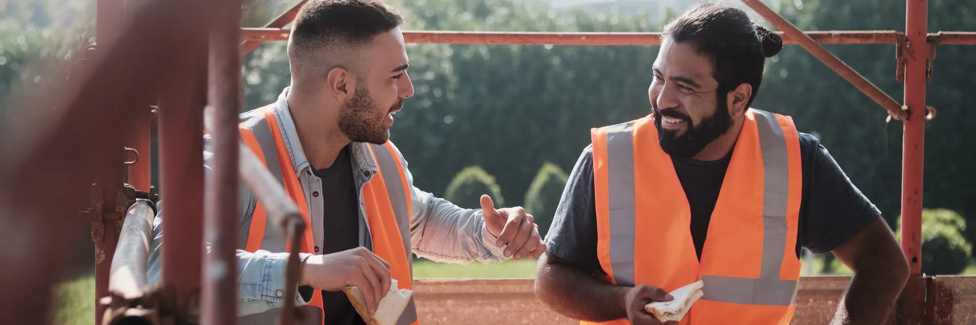 Hombres trabajando en un nuevo proyecto de vivienda. Equipo de trabajadores felices riendo, hablando y comiendo bocadillos durante el almuerzo.